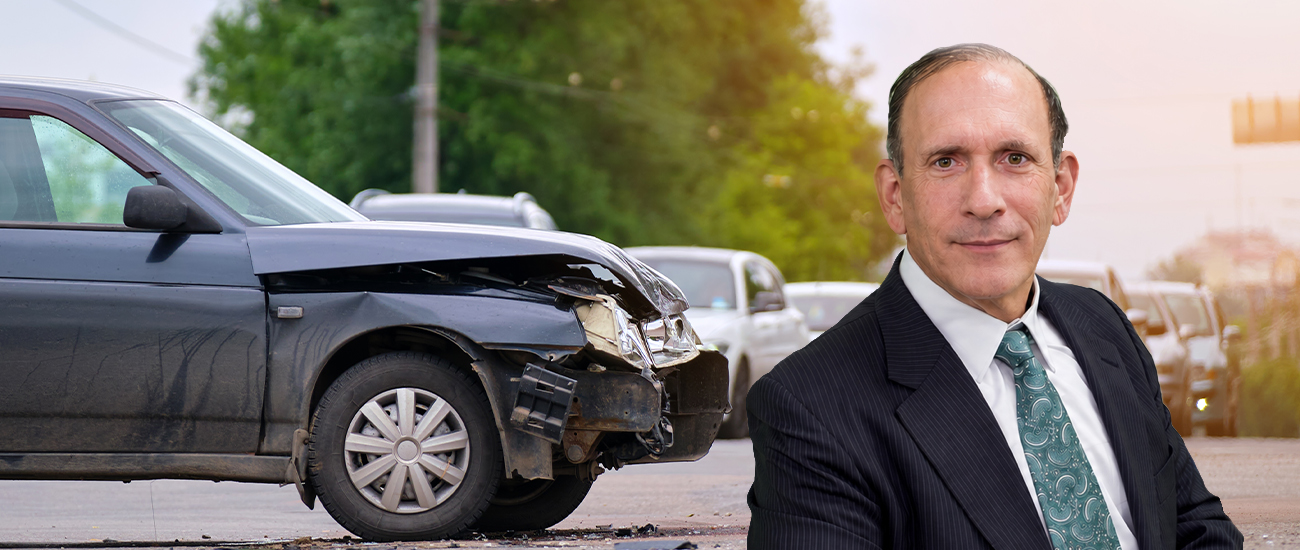 Attorney Dale Kasofsky stands beside a damaged car at the scene of a traffic accident.